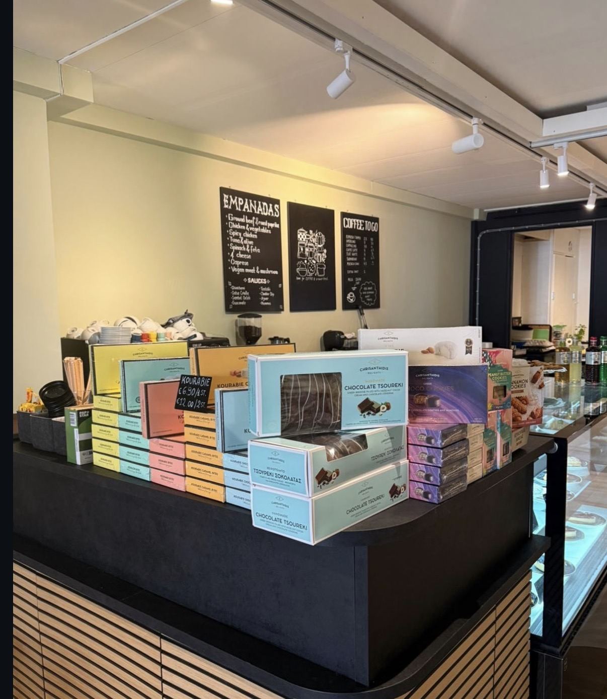 Inside Agora — the counter stacked with Greek sweets, chalkboard menus behind